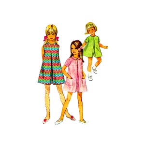 Peut inclure: Trois filles portant des robes. La fille à gauche porte une robe bleue, verte et rose à motif en zigzag. La fille du milieu porte une robe rose avec une fermeture éclair sur le devant. La fille à droite porte une robe à carreaux verts et blancs.