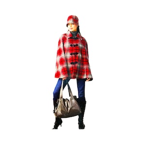 May include: A red and black plaid cape with black toggle closures, paired with a matching hat. The outfit is worn with blue jeans, black boots, and a brown handbag. The ensemble is set against a white background.