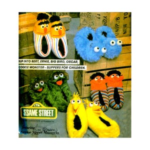 May include: A collection of Sesame Street character slippers for children, including Bert, Ernie, Cookie Monster, Oscar the Grouch, and Big Bird designs. The image features the text: SLIP INTO BERT, ERNIE, BIG BIRD, OSCAR, COOKIE MONSTER—SLIPPERS FOR CHILDREN.