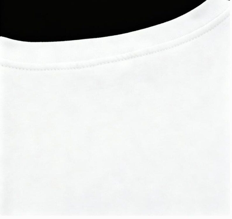 May include: Close-up of a white crew neck t-shirt. The neckline is visible, with a finely stitched seam. The fabric appears to be a soft, opaque material. The background is black.