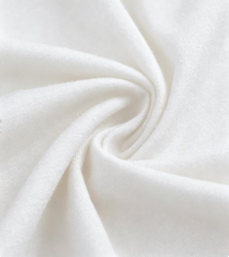 May include: Close-up of a white fabric with soft folds and a textured surface. The fabric appears to be tightly woven, with a subtle sheen. The image highlights the fabric's smooth texture and bright white color.