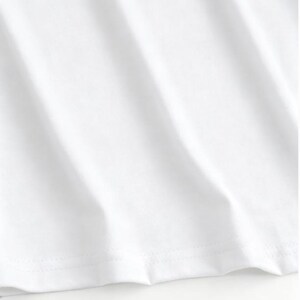 May include: Close-up of a white t-shirt, showing the fabric's texture and the stitched hemline. The fabric has subtle diagonal folds, creating shadows and highlights. The image focuses on the clean, crisp appearance of the garment.