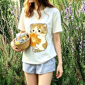 May include: A white t-shirt with a cartoon cat holding an orange slice. The cat is brown and white. The person is wearing blue and white striped shorts and holding a woven basket with lemons.