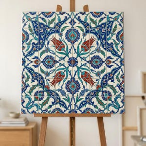 May include: A square wall art piece composed of twenty-five ceramic tiles featuring a symmetrical floral pattern. The design displays red tulips, blue swirling vines, and teal leaves against an off-white background, mounted on a wooden easel.