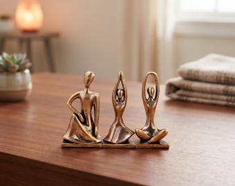 Könnte beinhalten: Ein Set aus drei bronzefarbenen Statuen, die Figuren in verschiedenen Yoga-Posen darstellen. Die Figuren sind auf einzelnen rechteckigen Sockeln montiert und weisen ein metallisches Finish mit dunklen Akzenten sowie glatte, abstrakte Formen auf.