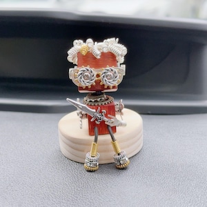 May include: A handcrafted robot figurine with a red wooden body, silver metal accents, and intricate gear details. The robot has a unique design with a sword and stands on a small wooden base. The robot's legs are gold and silver.
