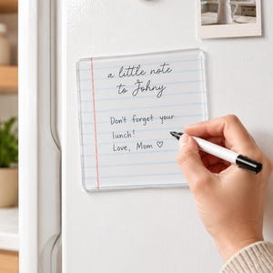 May include: A square clear acrylic dry-erase board with a printed notebook paper design featuring a red margin line and blue horizontal lines. The board displays the text: a little note to Johny, Don't forget your lunch! Love, Mom with a heart symbol.