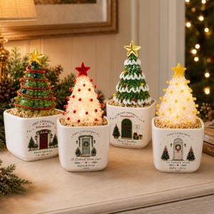 Puede incluir: Cuatro árboles de Navidad decorativos de mesa en macetas cuadradas de cerámica blanca. Cada árbol presenta un diseño único con una estrella en la punta y está personalizado con texto que incluye nombres, direcciones y el año 2026 en las macetas.