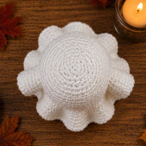 May include: A white crocheted octopus toy featuring a round, textured head and eight curled tentacles extending outward. The item is crafted from yarn with a consistent stitch pattern, displaying a soft, rounded shape viewed from directly above.