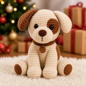 Puede incluir: Un peluche de perro tejido a ganchillo con cuerpo color crema y manchas marrones en una oreja, un ojo y las patas. El juguete tiene ojos de plástico negro, una nariz marrón y un collar marrón con una pequeña etiqueta circular marrón.