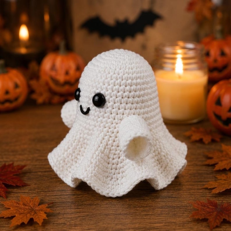May include: A small, white, crocheted ghost figurine featuring a rounded head, two small arms, and a flared base. The ghost has two smooth, black, circular plastic eyes and a small, black, stitched, curved mouth centered on its face.