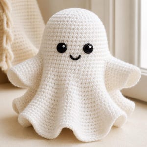 May include: A white crocheted ghost figure with a rounded head and a flared, wavy base. The ghost features two large, round, glossy black plastic safety eyes and a small, simple black embroidered mouth, creating a friendly facial expression.