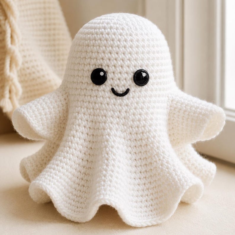 May include: A white crocheted ghost figure with a rounded head and a flared, wavy base. The ghost features two large, round, glossy black plastic safety eyes and a small, simple black embroidered mouth, creating a friendly facial expression.