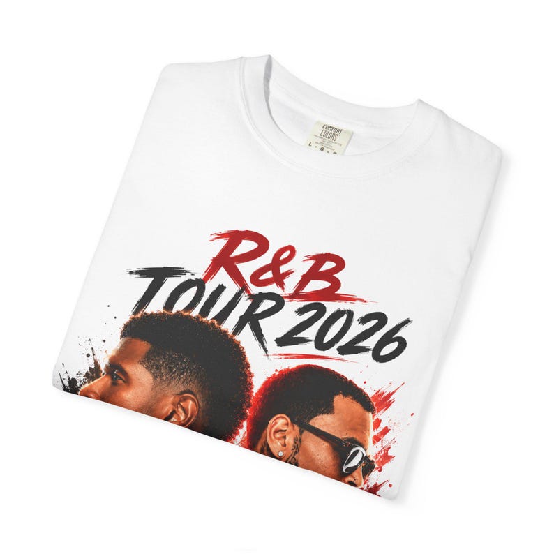 May include: A white t-shirt featuring a graphic print with the text R&B TOUR 2026 in red and black brushstroke lettering. Below the text are two portraits of individuals, one with a short haircut and one wearing sunglasses, accented by red paint splatters.