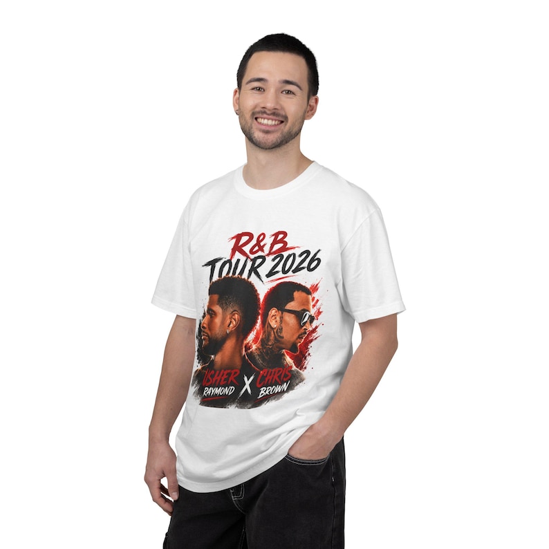 May include: A white short-sleeve t-shirt featuring a graphic print with the text R&B TOUR 2026, USHER RAYMOND, and CHRIS BROWN. The design includes portraits of two individuals back-to-back with red and black paint splatter accents.