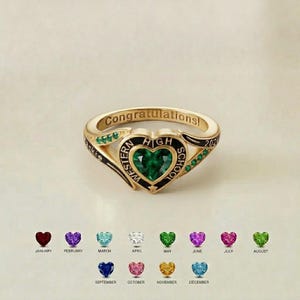 May include: A gold-colored ring with a heart-shaped green gemstone at the center. The ring is engraved with "Congratulations!" and "Western High School 202-". Below the ring are heart-shaped gemstones in various colors, each representing a month.