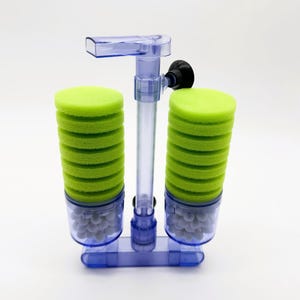 May include: A double sponge aquarium filter featuring two stacks of bright green circular foam pads mounted on a clear plastic frame. The base of each filter column contains small white ceramic bio-media balls, and a black suction cup is attached.