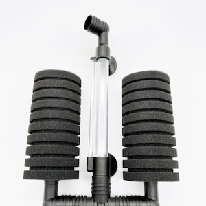 May include: A black double sponge aquarium filter featuring two cylindrical black foam sponges attached to a central plastic frame with a clear vertical tube and a black elbow-shaped outlet nozzle, including two small black suction cups for mounting.