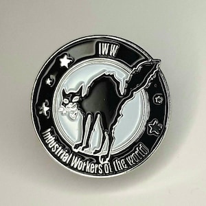 May include: Black and white enamel pin featuring a black cat silhouette and the text "IWW Industrial Workers of the World" around the edge.