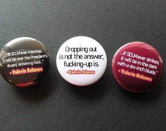 May include: Three round buttons with quotes by Valerie Solanos. One is black with white text, another is white with black text, and the third is maroon with white text. The buttons feature quotes about politics and failure.