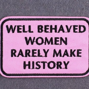 Peut inclure: Écusson en tissu rose avec du texte brodé en noir qui dit "Well Behaved Women Rarely Make History".