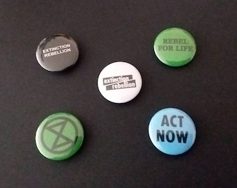 May include: Five round buttons with different messages and designs. The buttons are black, white, green, blue, and green. The messages on the buttons are "Extinction Rebellion", "extinction rebellion", "Rebel for Life", "Act Now", and a symbol with a circle around it.