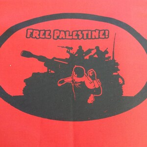 May include: A red t-shirt with a black oval graphic. The graphic features a tank, soldiers, and the text "FREE PALESTINE!"