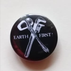 May include: Black and white button featuring a wrench and a pipe crossed over each other. The text "EARTH FIRST!" is written below the tools.