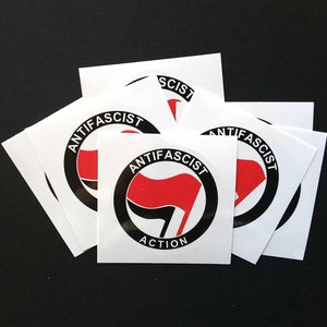Pode incluir: Uma coleção de adesivos quadrados brancos com um design de círculo preto. O design inclui uma bandeira vermelha e as palavras "ANTIFASCIST ACTION" em texto preto. Os adesivos estão em um fundo preto.