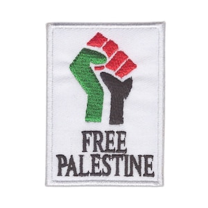 Może przedstawiać: Biała łatka z uniesioną w górę czarną, zieloną i czerwoną pięścią. Pod pięścią znajduje się napis "FREE PALESTINE".