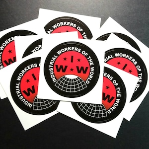 May include: A stack of white stickers with a black and red circular logo. The logo says "Industrial Workers of the World" with a red star and the letters "IWW" inside a red circle. The circle is on top of a black globe with a white grid.