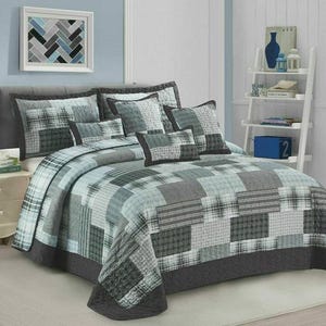 May include: A bed featuring a patchwork quilt in shades of grey, blue, and white. The quilt has various patterns and textures. Matching pillows and a bed skirt complete the set. A framed artwork hangs above the bed.
