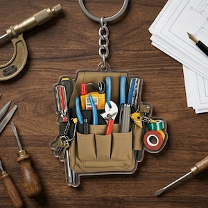 May include: A tool-themed keychain featuring a miniature tool bag filled with various tools like screwdrivers, pliers, and a wrench. The keychain is set on a wooden surface alongside a micrometer, files, and a pen with blueprints.