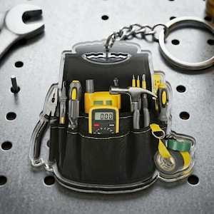 May include: A clear acrylic keychain shaped like a tool belt, filled with miniature tools. The tools include pliers, screwdrivers, a hammer, and a multimeter. The keychain has a silver chain and ring for attaching to keys.