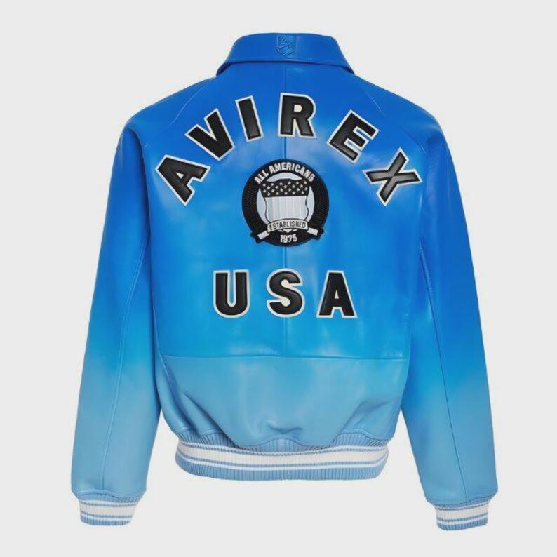 May include: Blue leather jacket with the word "AVIREX" arched across the shoulders in black lettering. Below the lettering is a circular patch with the words "All Americans Established 1975". The word "USA" is printed in white block letters below the patch. The jacket has a gradient color scheme.