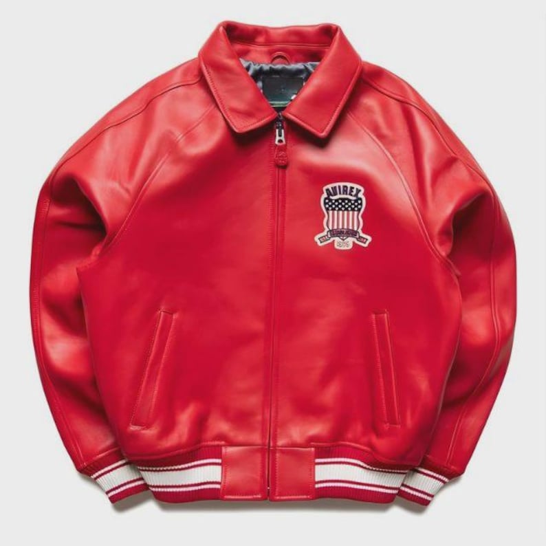 May include: A vibrant red leather jacket with a collared neckline and a zip-up front. The jacket features a white and red striped hem and cuffs, and a patch on the chest with the text "AVIREX".