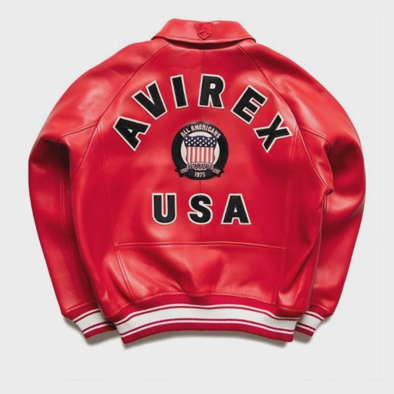May include: A red leather jacket with the word "AVIREX" arched across the back in black block letters. Below the word is a circular patch with the words "ALL AMERICANS" and "USA" in white. The jacket has a white and red striped trim.