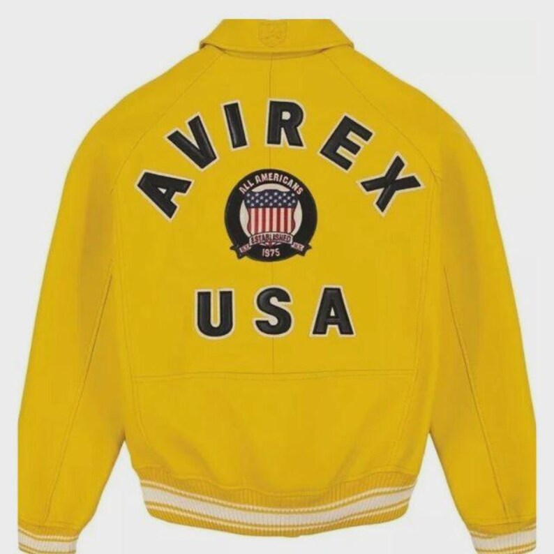 May include: Yellow bomber jacket with the word "AVIREX" across the back in black block letters. Below the word "AVIREX" is a circular patch with the words "ALL AMERICANS" and "1975" and a USA flag design. The word "USA" is below the patch.