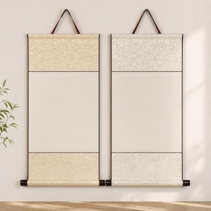 May include: Two rectangular wall scrolls with a cream-colored textured top and bottom section, and a plain off-white center. The scrolls have dark brown wooden dowels at the bottom and are suspended by brown leather straps.