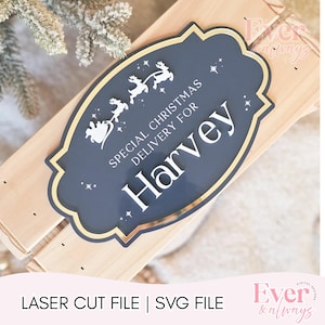 Könnte beinhalten: Ein marineblaues Weihnachtsschild mit goldenem Rand und dem Text "SPECIAL CHRISTMAS DELIVERY FOR Harvey". Das Schild zeigt eine Silhouette des Weihnachtsschlittens und der Rentiere. Das Schild befindet sich auf einer Holzoberfläche.