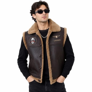 May include: A dark brown sleeveless waistcoat with a tan faux fur lining and collar. The garment features a button-up front, two side pockets, and two embroidered patches on the chest: a skull design on the right and a winged emblem on the left.