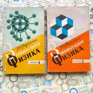 Puede incluir: Dos libros antiguos titulados "Занимательная Физика" de Ya. I. Perelman. El libro de la izquierda tiene una cubierta verde claro con un gráfico de engranaje verde oscuro y una sección amarilla. El de la derecha es gris claro con cubos azules.