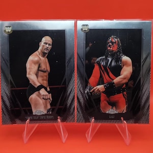 May include: Two wrestling trading cards on display. One card features "Stone Cold" Steve Austin in black trunks. The other card shows Kane in a red and black outfit. Both cards have the Topps Chrome logo.