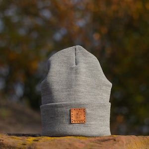 Op de afbeelding: Grijze beanie met een bruin leren patch waarop "ALIEN" en "THE TRUTH IS OUT THERE" staat.