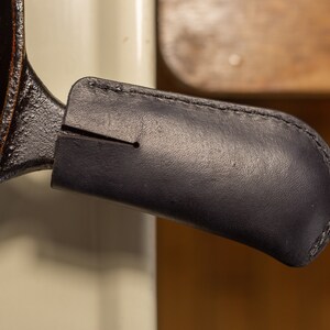 May include: A black cast iron skillet with a dark brown leather handle cover.