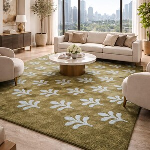 May include: A living room with a large olive green rug featuring a repeating white leaf pattern. The room includes a white sofa, two armchairs, a round coffee table, and a large window with a city view.