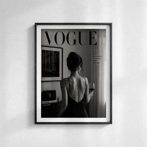 Puede incluir: Impresi&oacute;n enmarcada en blanco y negro con el logotipo de Vogue. La imagen muestra a una mujer con un vestido negro sosteniendo una copa de vino tinto. El texto dice: "La belleza comienza en el momento en que decides ser t&uacute; mismo".