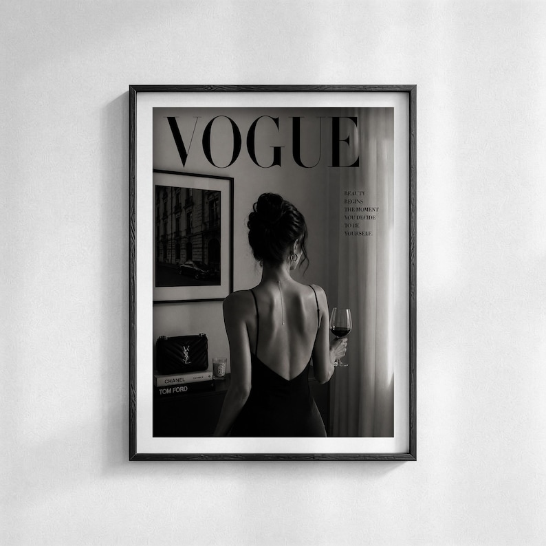 Puede incluir: Impresi&oacute;n enmarcada en blanco y negro con el logotipo de Vogue. La imagen muestra a una mujer con un vestido negro sosteniendo una copa de vino tinto. El texto dice: "La belleza comienza en el momento en que decides ser t&uacute; mismo".