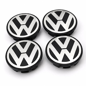 May include: Four black and silver Volkswagen wheel center caps. Each cap features the VW logo in silver against a black background. The caps are round and have a black outer ring.