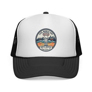 May include: Black and white trucker hat with a white front panel featuring a circular graphic for the FIFA World Cup 2026. The graphic includes the World Cup trophy, a cityscape, and the text "North America Canada-Mexico-USA."